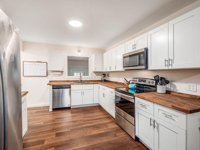 kitchen with dark wood-style floors, stainless steel appliances, butcher block counters, white cabinetry, and a sink