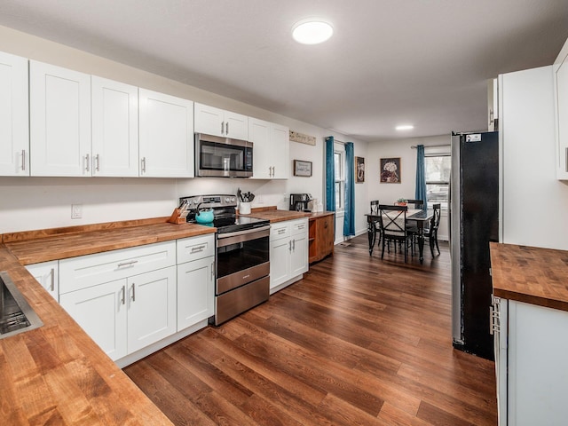 kitchen with dark wood finished floors, stainless steel appliances, butcher block counters, white cabinetry, and a sink