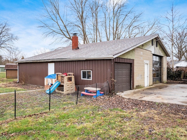 exterior space featuring a garage, a chimney, roof with shingles, an outbuilding, and fence