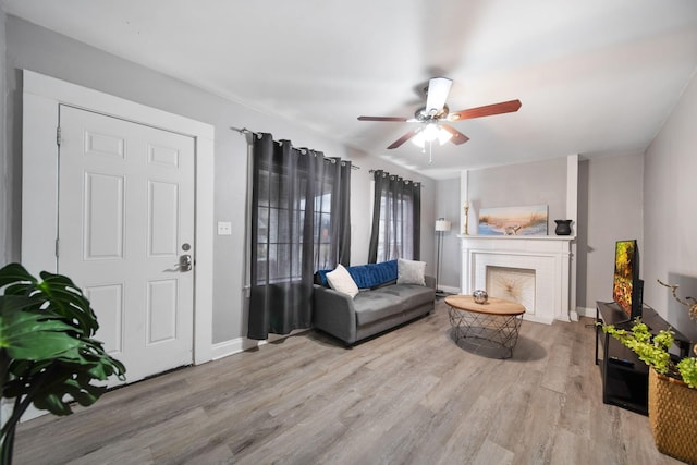 living room featuring a brick fireplace, wood finished floors, a ceiling fan, and baseboards