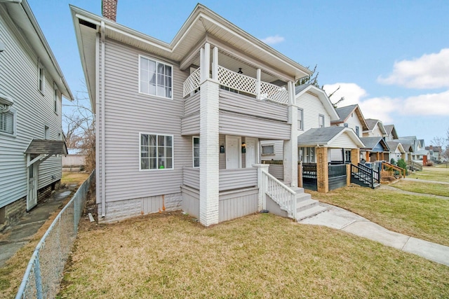 view of front of property featuring a porch, a balcony, a residential view, a front lawn, and a chimney