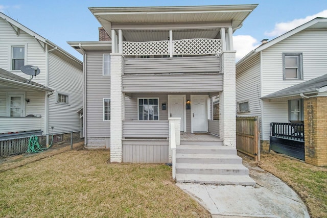 view of front of home with a balcony, covered porch, fence, and a front lawn