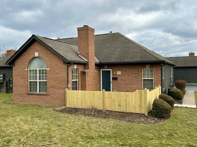 rear view of property featuring brick siding, a chimney, a shingled roof, a lawn, and fence