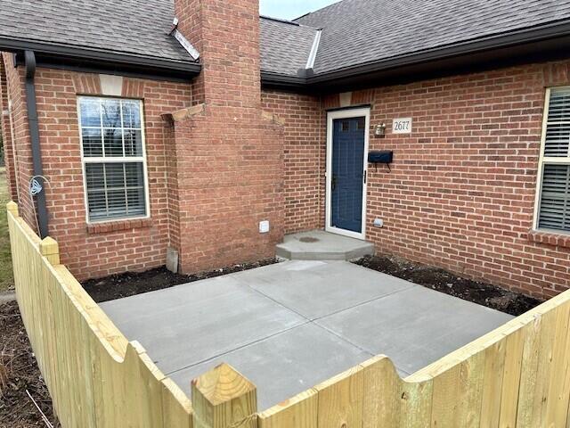 entrance to property with a shingled roof, a chimney, and brick siding