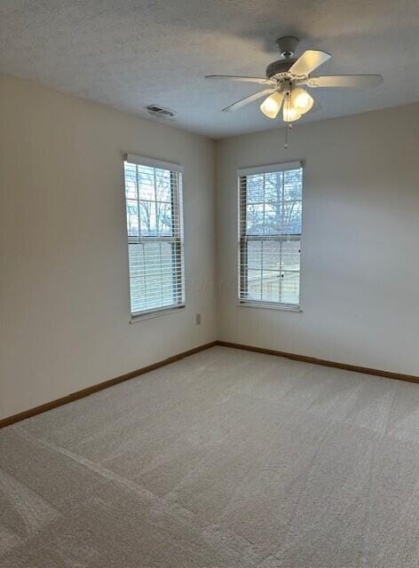 empty room featuring a textured ceiling, baseboards, visible vents, and light colored carpet