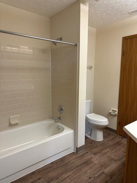 full bath featuring toilet, a textured ceiling, visible vents, and wood finished floors