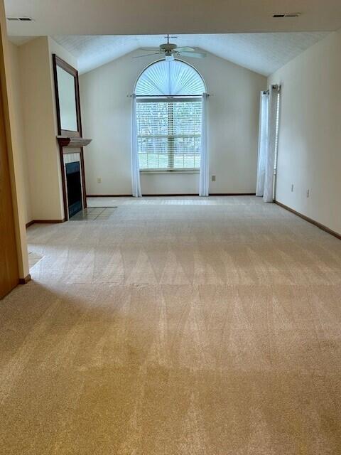 unfurnished living room with light colored carpet, visible vents, vaulted ceiling, and ceiling fan