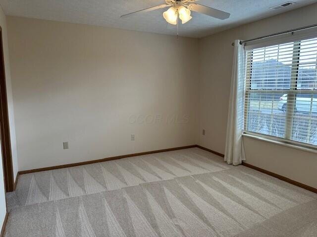 empty room featuring light carpet, a textured ceiling, visible vents, and baseboards