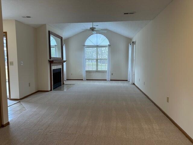 unfurnished living room featuring light carpet, visible vents, a tiled fireplace, ceiling fan, and vaulted ceiling