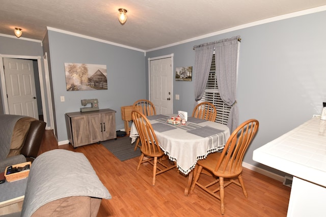 dining space with baseboards, ornamental molding, a textured ceiling, and light wood-style floors