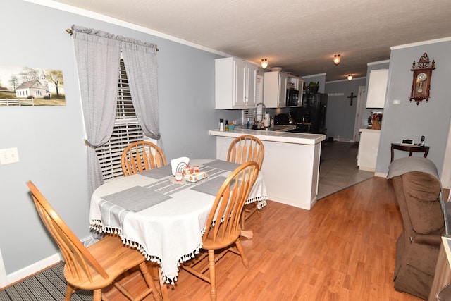 dining space featuring a textured ceiling, baseboards, light wood-style flooring, and crown molding