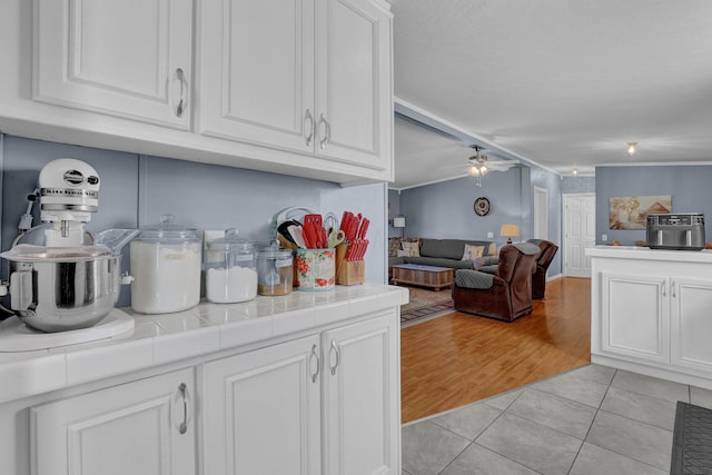 kitchen with tile counters, open floor plan, light tile patterned floors, white cabinetry, and a ceiling fan