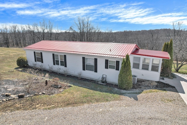view of front of house featuring a forest view, metal roof, central AC, and a front yard