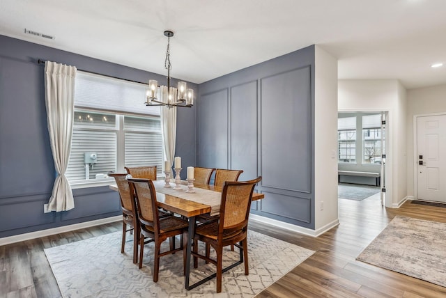 dining area featuring visible vents, wood finished floors, a decorative wall, baseboards, and a chandelier