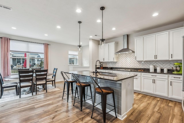 kitchen featuring visible vents, light wood-style flooring, wall chimney range hood, and a sink