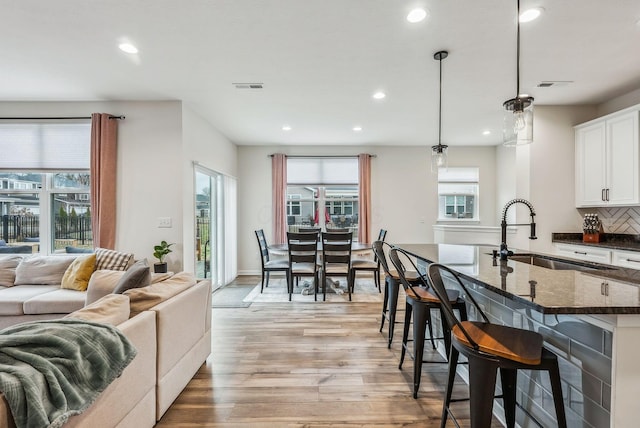 kitchen featuring visible vents, open floor plan, dark stone counters, light wood-style floors, and a sink