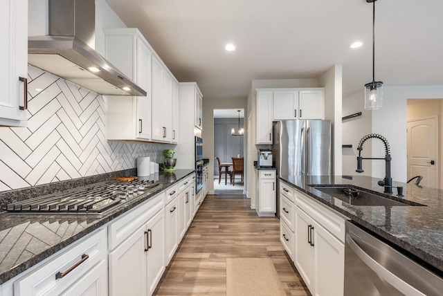 kitchen with a sink, white cabinetry, light wood-style floors, appliances with stainless steel finishes, and wall chimney exhaust hood