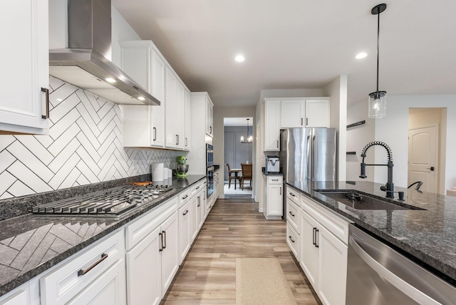 kitchen featuring wall chimney range hood, appliances with stainless steel finishes, light wood-style floors, white cabinetry, and a sink