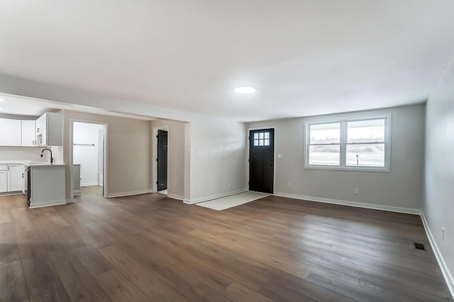 unfurnished living room with dark wood-style floors, a sink, visible vents, and baseboards