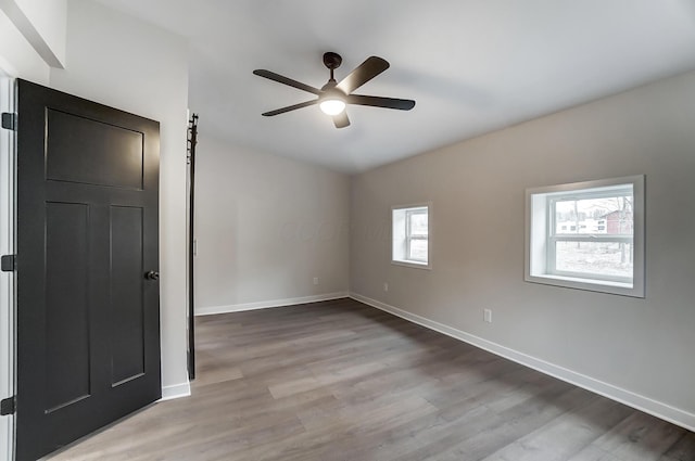 spare room featuring a ceiling fan, a barn door, baseboards, and wood finished floors