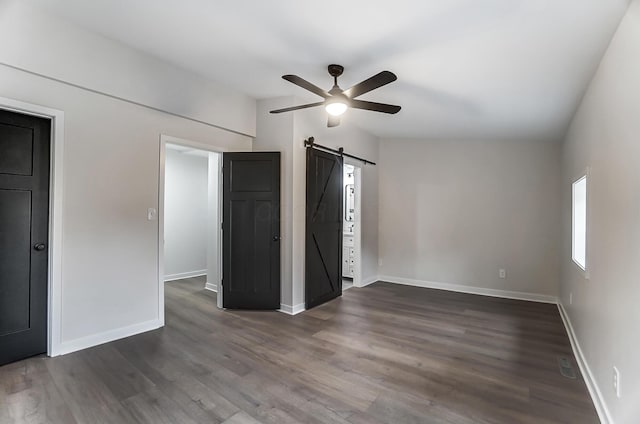 unfurnished bedroom with a barn door, baseboards, ceiling fan, and dark wood-style flooring