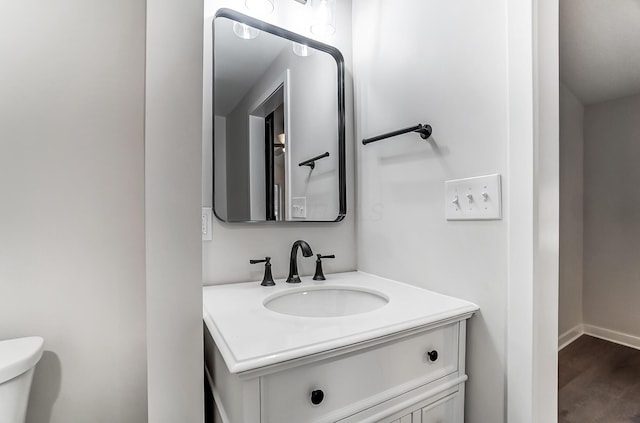 bathroom with toilet, wood finished floors, vanity, and baseboards