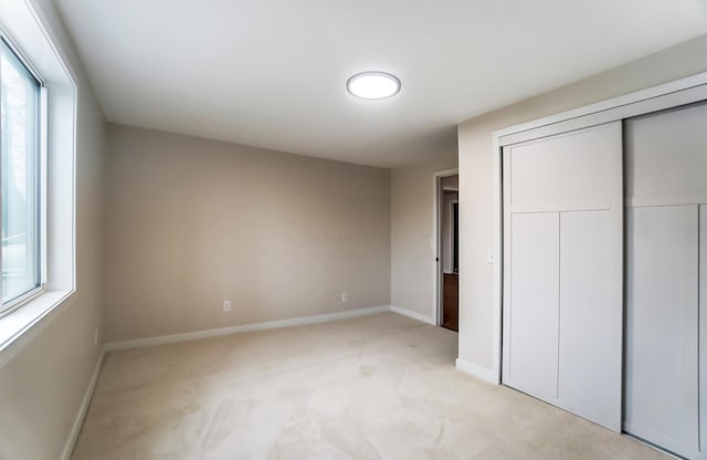 unfurnished bedroom with light carpet, baseboards, and a closet