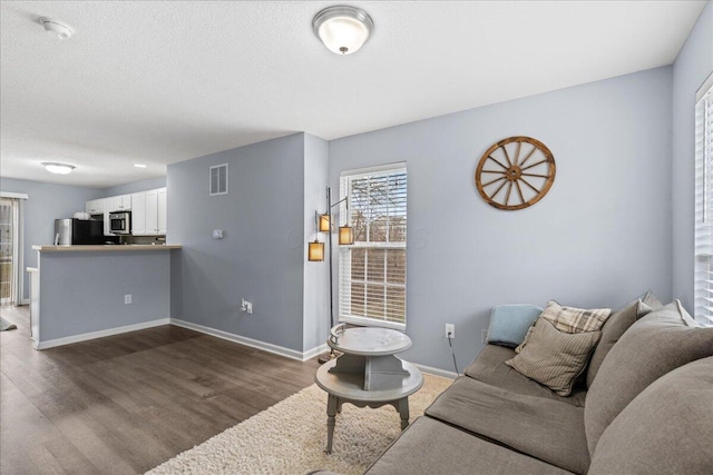 living room featuring visible vents, baseboards, dark wood-type flooring, and a textured ceiling