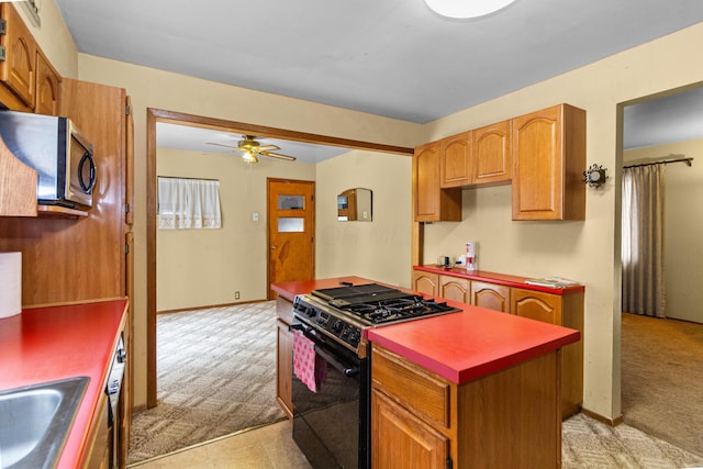 kitchen featuring range with gas stovetop, light colored carpet, ceiling fan, stainless steel microwave, and a center island