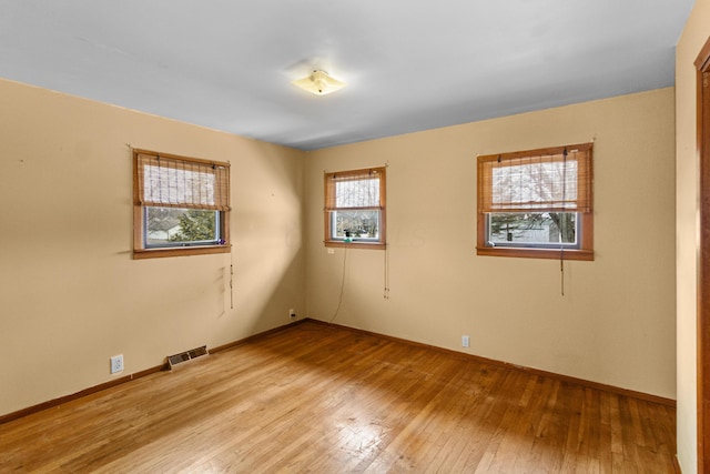 spare room featuring wood-type flooring, visible vents, and baseboards