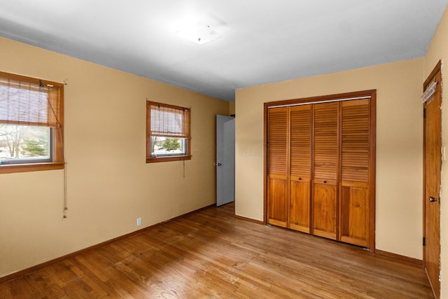 unfurnished bedroom featuring light wood-style floors, a closet, multiple windows, and baseboards