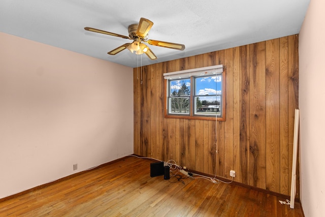 empty room featuring hardwood / wood-style flooring, ceiling fan, and wooden walls