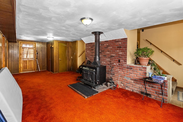 living area with a wood stove, carpet flooring, a textured ceiling, and stairs