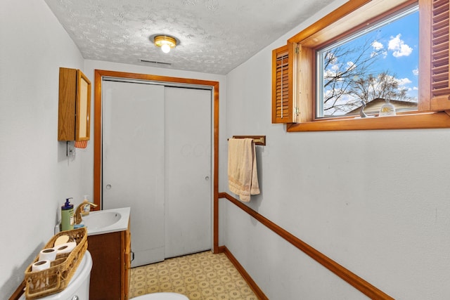 bathroom with toilet, a textured ceiling, vanity, baseboards, and tile patterned floors