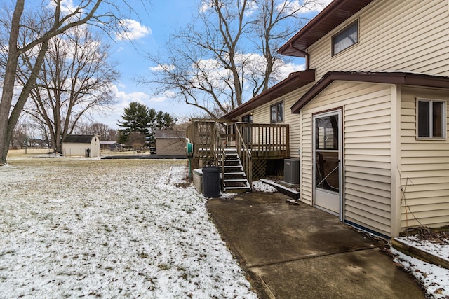 yard covered in snow with a deck, central AC, an outdoor structure, and stairs