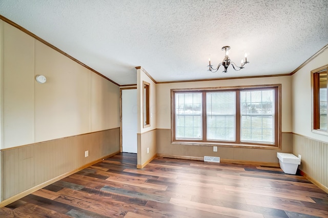 spare room with a textured ceiling, wainscoting, wood finished floors, and visible vents