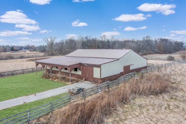 exterior space featuring metal roof, a rural view, an outdoor structure, driveway, and an exterior structure