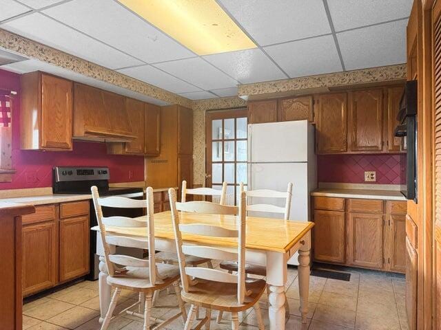 kitchen with brown cabinetry, a drop ceiling, stainless steel electric range oven, freestanding refrigerator, and light countertops