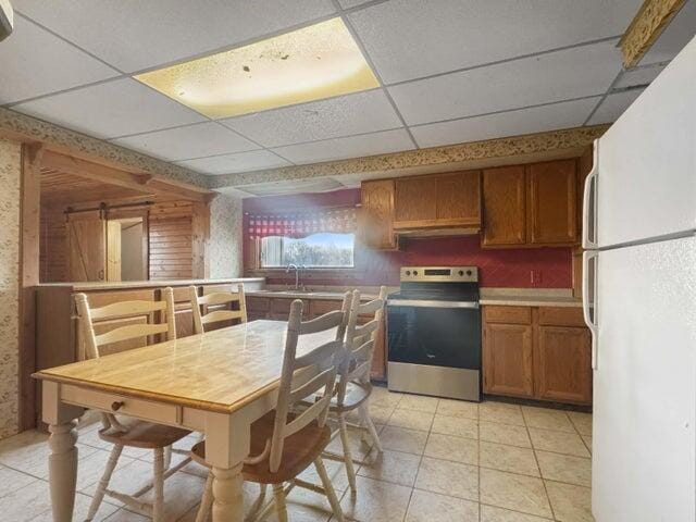 kitchen featuring brown cabinets, freestanding refrigerator, stainless steel electric range, a paneled ceiling, and light tile patterned flooring
