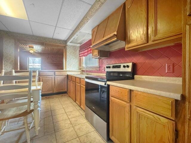 kitchen featuring light tile patterned floors, light countertops, stainless steel range with electric cooktop, a sink, and a drop ceiling