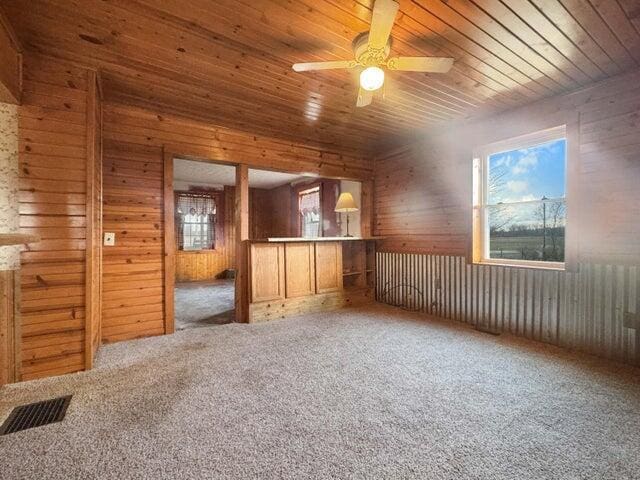 carpeted empty room featuring wood ceiling, ceiling fan, wood walls, and visible vents