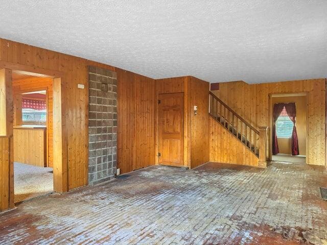 unfurnished living room featuring a textured ceiling, stairway, and wood walls