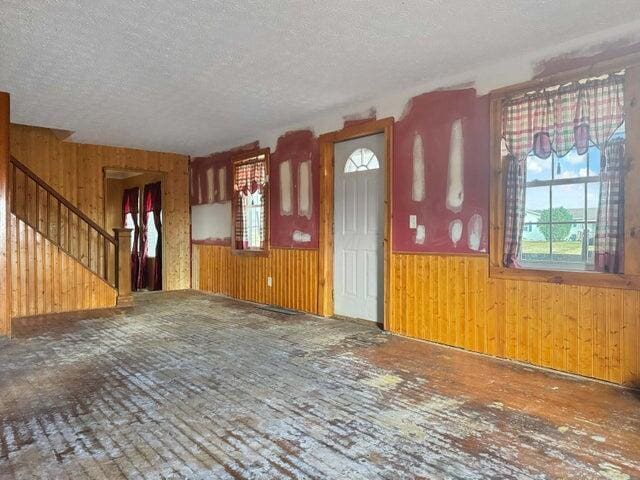 unfurnished living room featuring a wainscoted wall, stairway, wood walls, and a textured ceiling