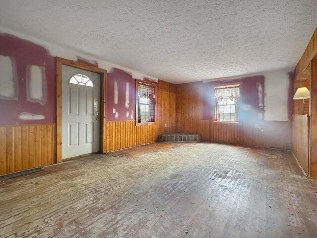 unfurnished living room with wainscoting, wooden walls, and a textured ceiling