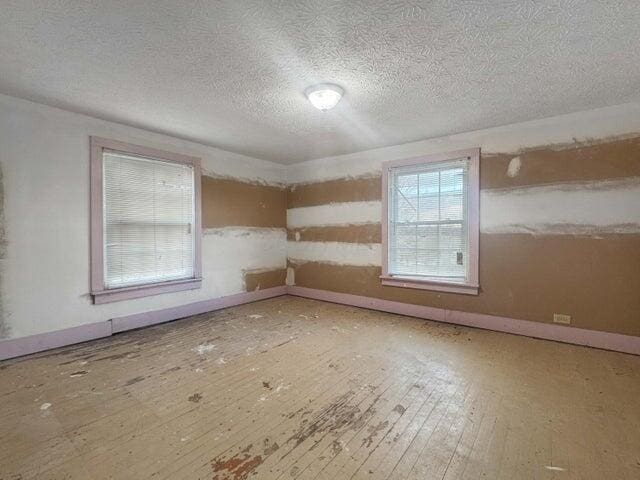 unfurnished room featuring a textured ceiling, baseboards, and hardwood / wood-style flooring