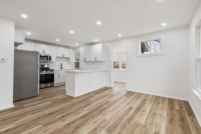 kitchen with a peninsula, white cabinets, light countertops, appliances with stainless steel finishes, and decorative backsplash