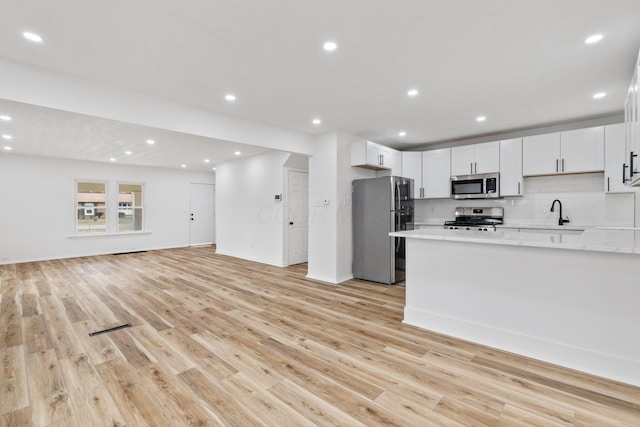 kitchen with stainless steel appliances, open floor plan, light wood-style floors, and decorative backsplash