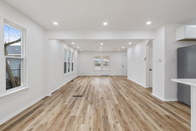 unfurnished living room with light wood finished floors, a wealth of natural light, and recessed lighting