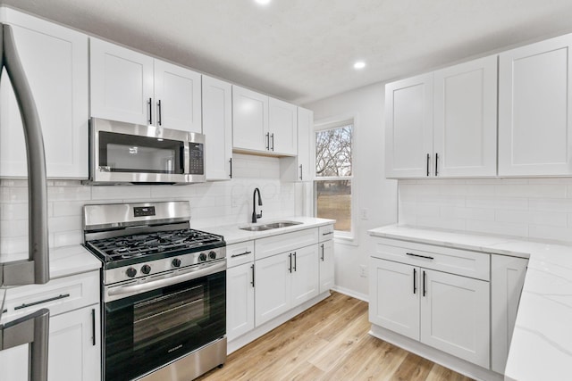 kitchen featuring white cabinets, light wood finished floors, stainless steel appliances, and a sink