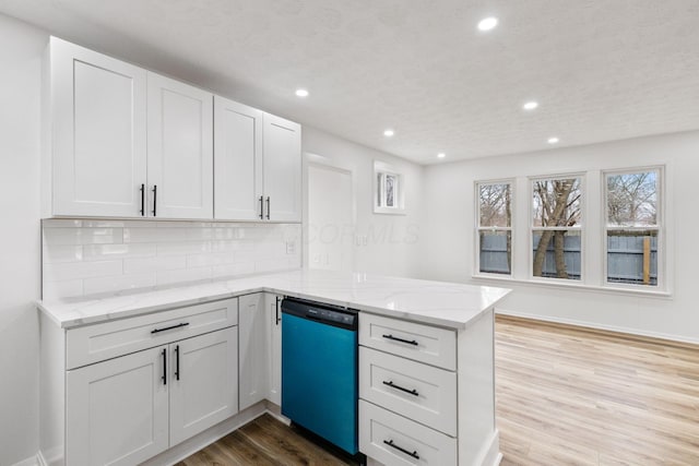 kitchen featuring backsplash, light stone countertops, light wood-type flooring, a peninsula, and dishwashing machine